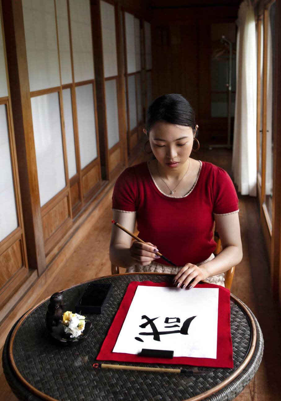 A woman is successfully writing Chinese calligraphy at a table with coaching support.